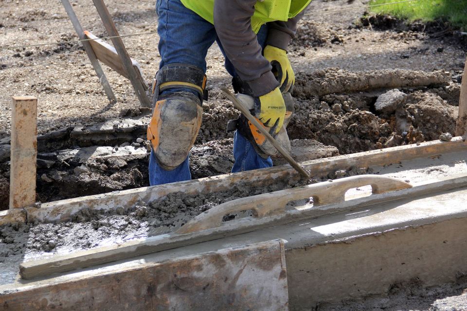 Concrete being leveled beside timber formwork with a hand tool